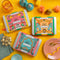 Three Spice Kitchen Feasting Kit tins on a yellow surface with decorative items.