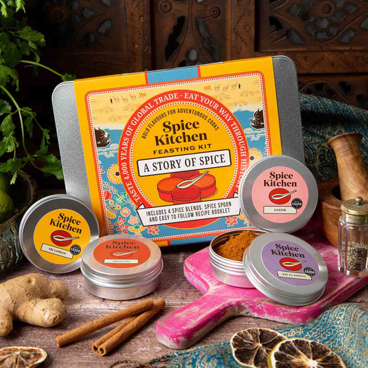 Spice Kitchen's Feasting Tin – A Story of Spice' with four signature spice blends on a wooden chopping board with spices and silk sari material. 