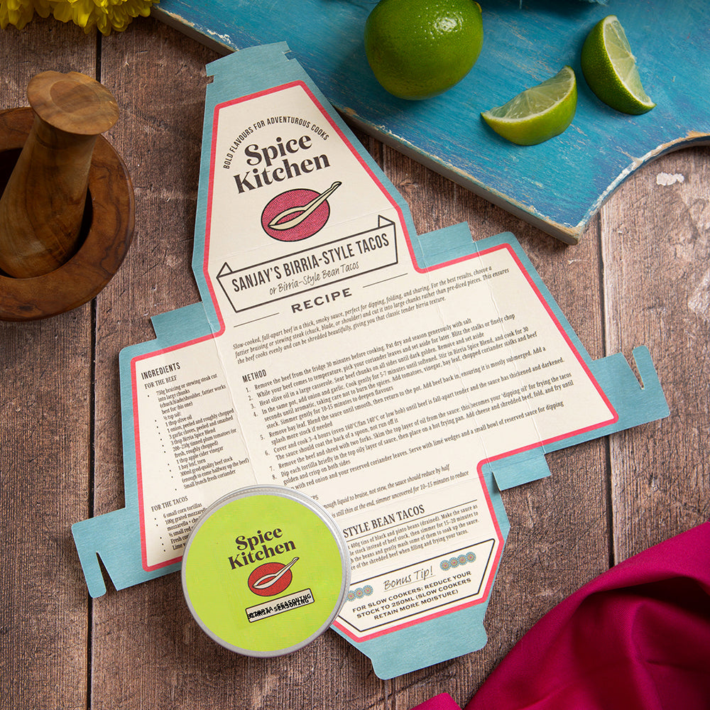 Sanjay's Birria Taco Recipe on a wooden board with decorative kitchen items and a spice blend pot