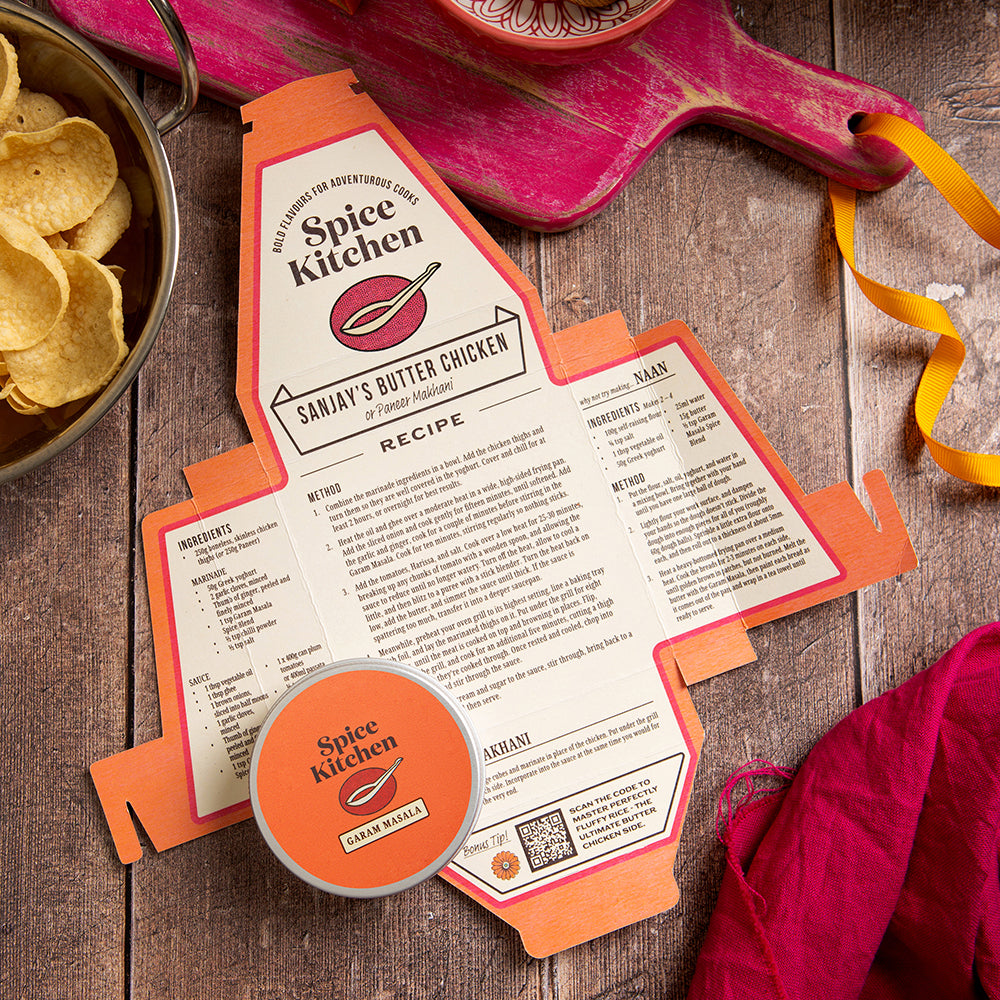Sanjay's Butter Chicken recipe card on a wooden board with a spice spoon, poppadoms and Garam Masala spice blend in a pot. 