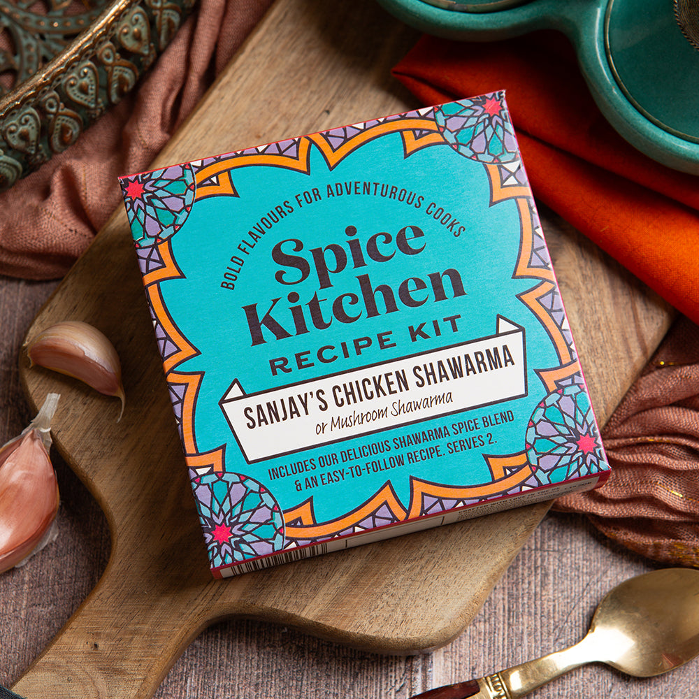 Spice Kitchen Recipe Kit for Sanjay's Chicken Shawarma on a wooden board with garlic and a spoon.