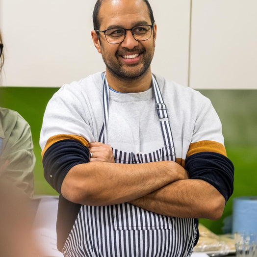 Sanjay wearing a striped apron and glasses in a kitchen setting