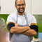Sanjay wearing a striped apron and glasses in a kitchen setting