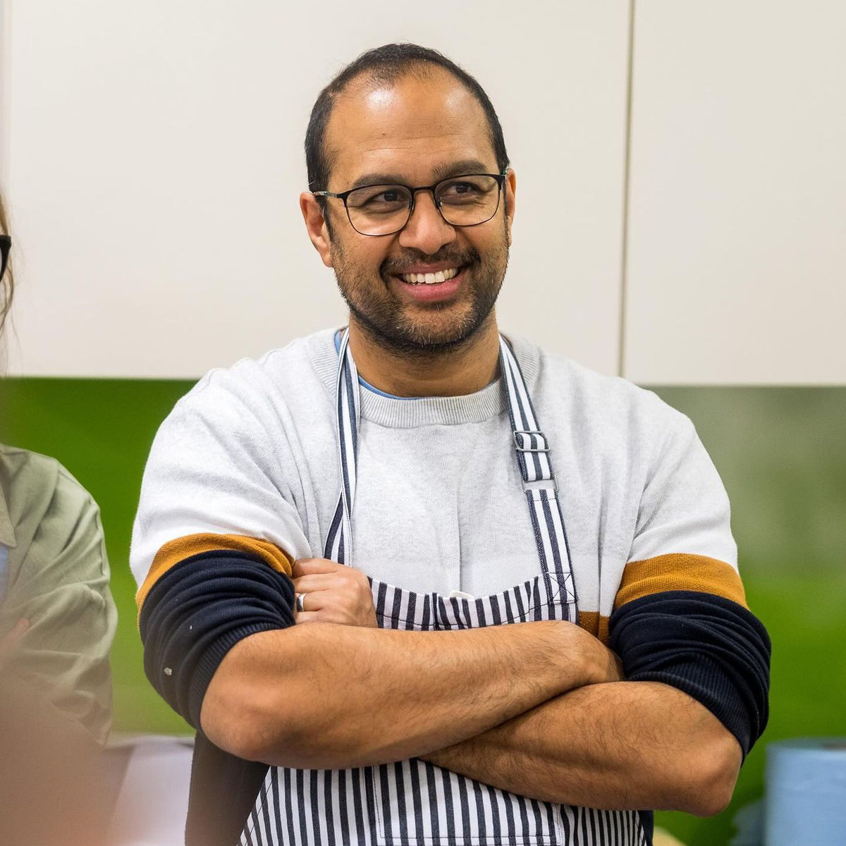 Sanjay wearing a striped apron and glasses in a kitchen setting