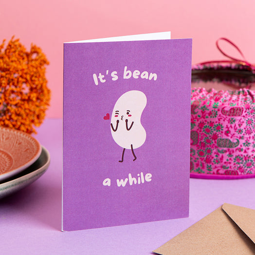 Purple card with a cartoon character and text 'It's bean a while' on a pink background
