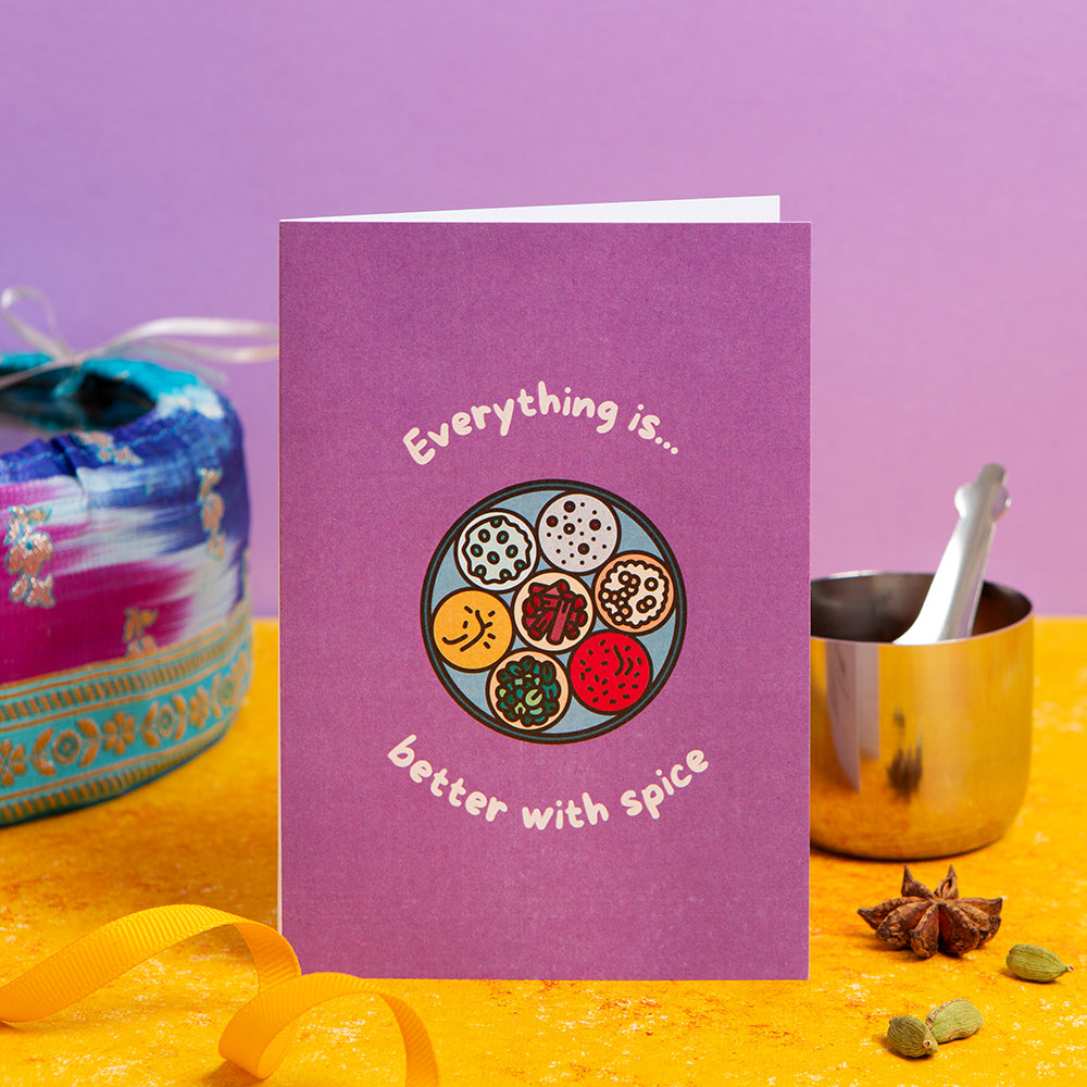 Purple card with spice-themed design on a yellow surface with spices and containers.