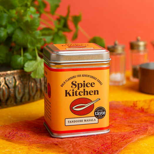 Spice Kitchen Tandoori Masala can on a colorful background with plants and other spices.