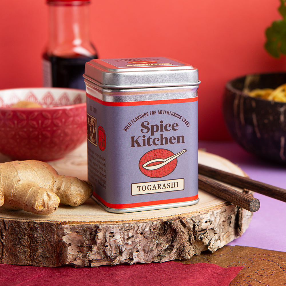 Spice Kitchen Togarashi spice tin on a wooden surface with ginger and chopsticks.