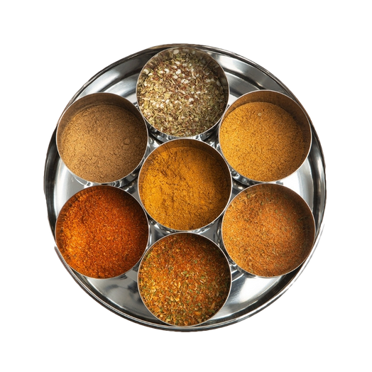 A top-down view of a round silver metal spice tray with seven small inner tins filled with different ground spices in warm brown, orange, and yellow tones.